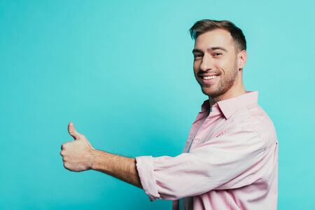 happy handsome man showing thumb up, isolated on blue