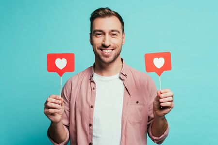 smiling man holding cards with hearts for valentines day, isolated on blue