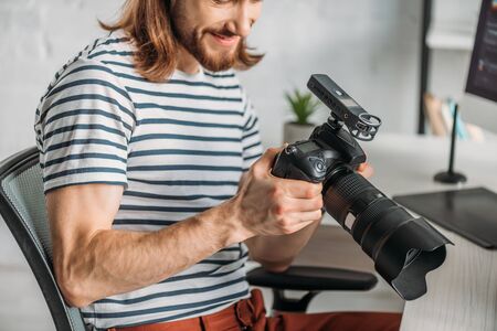 cropped view of happy editor holding digital camera