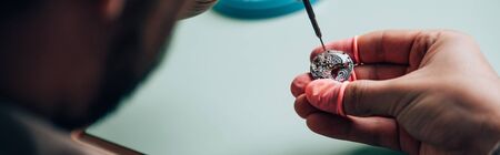 Panoramic shot of watchmaker in latex fingertips setting wristwatch detail with screwdriver