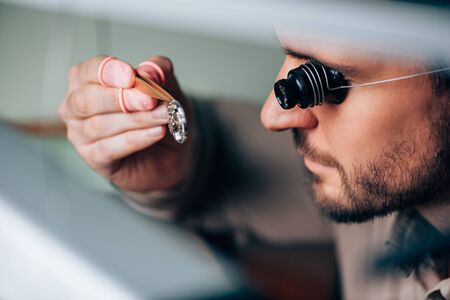 Side view of handsome watchmaker in eyeglass loupe looking at wristwatch part
