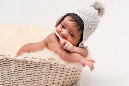cute newborn mixed race baby touching knitted hat on white