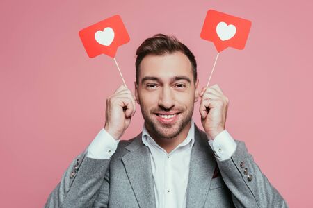 smiling man holding cards with hearts for valentines day, isolated on pink