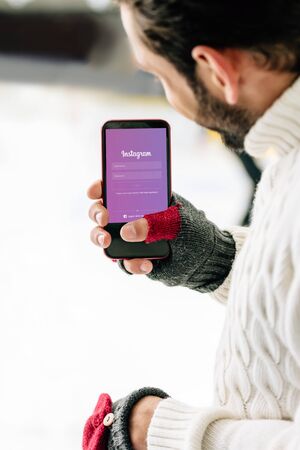 KYIV, UKRAINE - NOVEMBER 15, 2019: cropped view of man in gloves holding smartphone with instagram app on screen, on skating rinkのeditorial素材