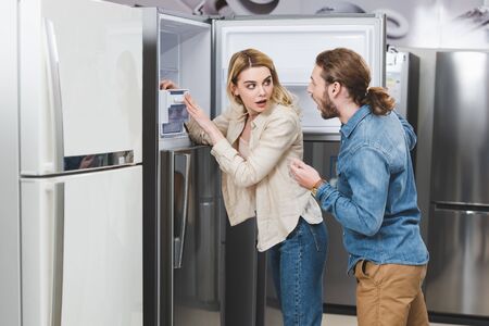 shocked boyfriend and girlfriend standing near fridge in home appliance storeの写真素材