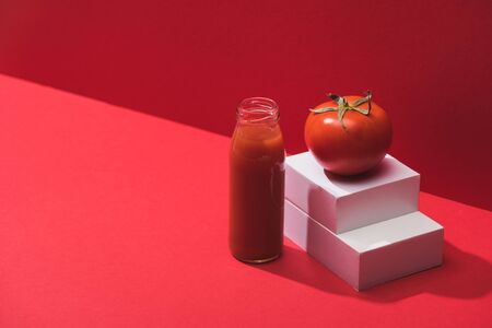fresh vegetable juice in glass bottle near ripe tomato on stand on red backgroundの写真素材