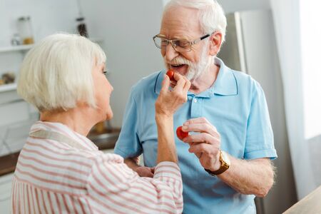 Selective focus of senior couple holding ripe cherry tomatoes in kitchen