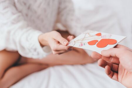 cropped view of woman taking greeting card with hearts for valentines day from man on bedの写真素材