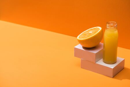 fresh juice in glass bottle near orange half and white cubes on orange backgroundの写真素材