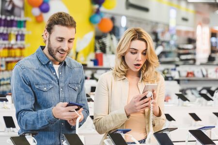 shocked boyfriend and girlfriend looking at new smartphones in home appliance store