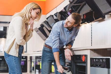 smiling consultant showing oven to pensive woman in home appliance storeの写真素材