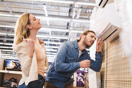 boyfriend looking at air conditioner and smiling girlfriend cooling in home appliance storeの写真素材