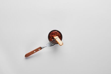 Top view of slice of steak on fork by tomato sauce on white background