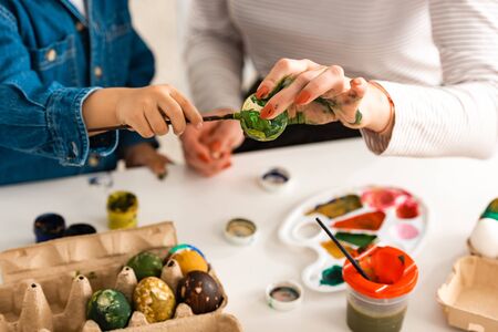 cropped view of mother and son sitting at table and painting Easter eggsの写真素材