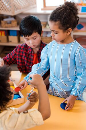 Selective focus of kids with hourglass and board game during lesson in montessori school