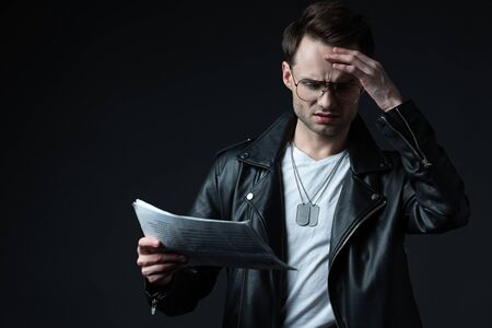 worried stylish brutal man in biker jacket with newspaper isolated on black