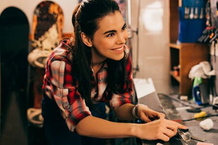 smiling worker repairing ski and looking away in repair shop