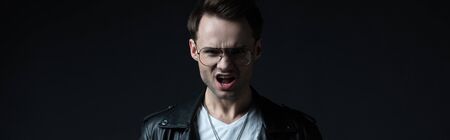 stylish brutal man in biker jacket screaming isolated on black, panoramic shot