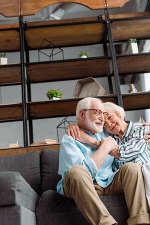 Low angle view of smiling senior couple hugging on couch at homeの写真素材