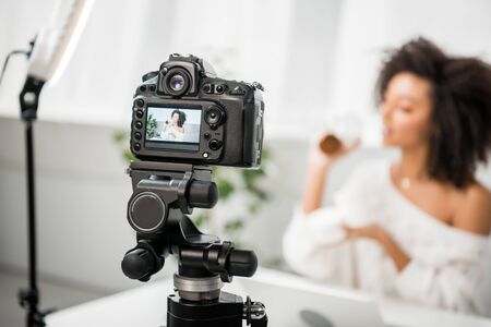 selective focus of digital camera with african american influencer holding containers with face...