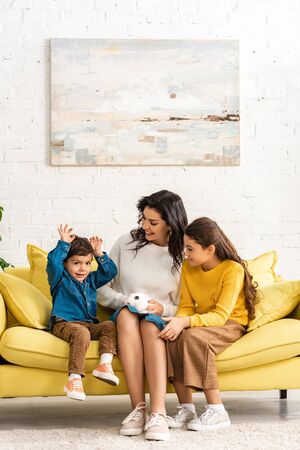happy children and cheerful mother sitting on sofa with white funny rabbit