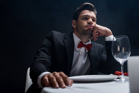 Selective focus of handsome man in suit sitting at served table isolated on black