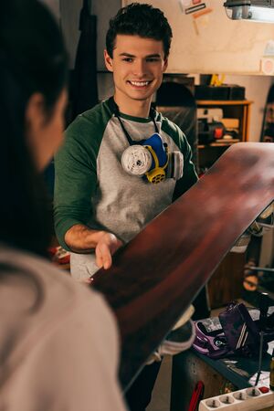 cropped view of woman giving snowboard to smiling worker in repair shopの写真素材