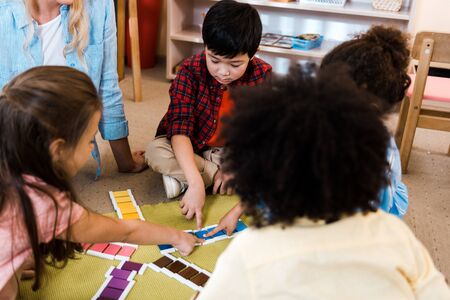Selective focus of kids folding colorful game by teacher on floor in montessori school