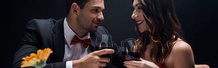 Panoramic shot of elegance couple with wine glasses smiling at each other isolated on black