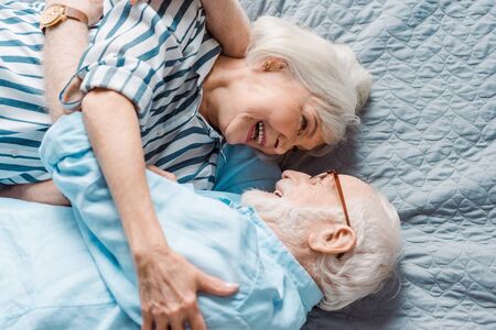 Top view of elderly couple smiling at each other on bedの写真素材