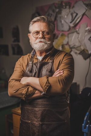 smiling, bearded cobbler standing with crossed arms and looking at camera