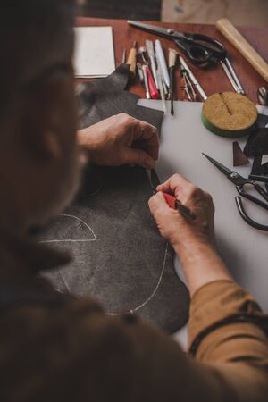cropped view of cobbler cutting genuine leather with knife in workshop