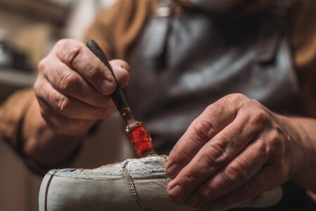 cropped view of shoemaker applying glue on shoe with brushの写真素材