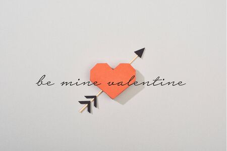 Top view of decorative paper heart with arrow and be mine valentine lettering on grey background