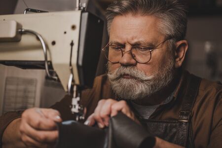 senior, bearded cobbler sewing leather on sewing machineの写真素材
