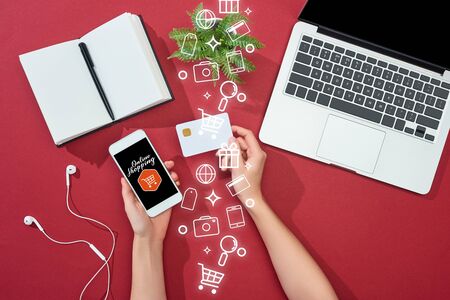 cropped view of woman holding credit card and smartphone with online shopping illustration near...