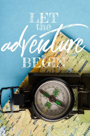 top view of black compass on map near let the adventure begin letters on blue