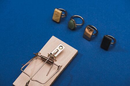 High angle view of wooden mouse trap with jewellery rings on blue backgroundの写真素材