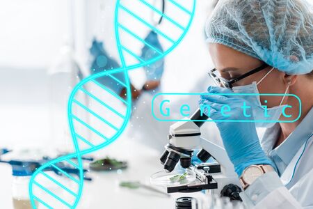 selective focus of biologist looking through microscope and sitting near genetic illustration