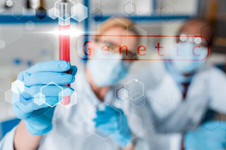 selective focus of multicultural biologists looking at test tube with genetic illustration