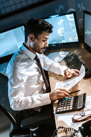 bi-racial trader using calculator and holding charts and graphs near money signsの写真素材