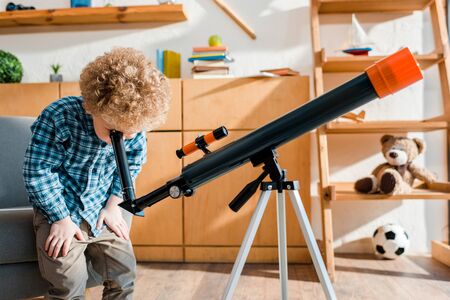 smart child in plaid shirt looking through telescope