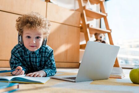 selective focus of smart child listening music in wireless headphones while holding pen near laptop