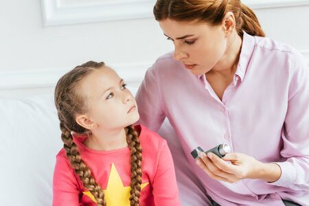 worried mother giving inhaler to sad daughter with asthma