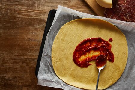 Top view of raw dough with tomato sauce on wooden backgroundの写真素材
