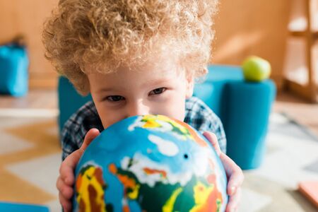 selective focus of smart kid holding globe and looking at camera