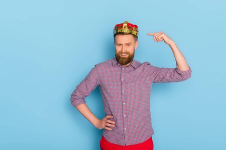 smiling man pointing with finger at crown on blue background