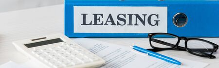 panoramic shot of folder with leasing lettering near calculator, pen and glasses on deskの写真素材