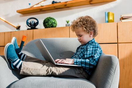 cute kid sitting in armchair and using laptopの写真素材