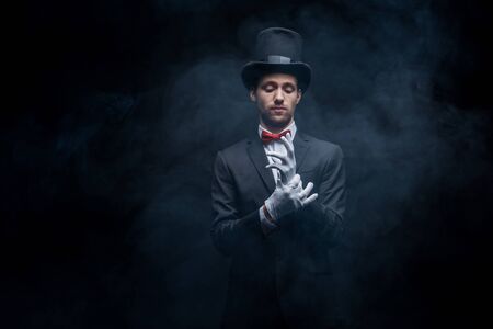 magician in suit and hat wearing gloves in dark smoky room